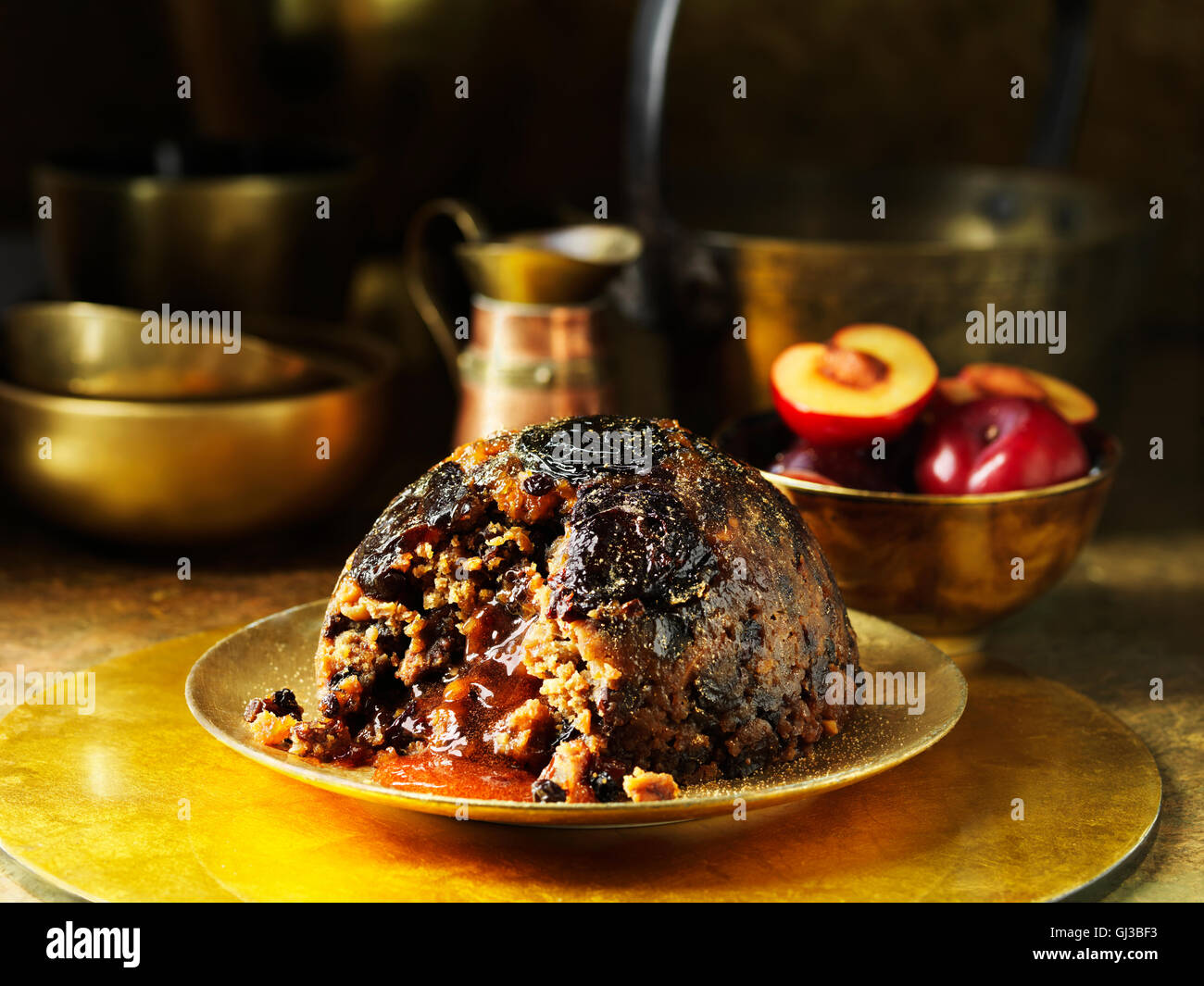 Sugar plum-pudding sur plaque dorée, prunes fraîches en arrière-plan, Métal pots et casseroles en arrière-plan Banque D'Images