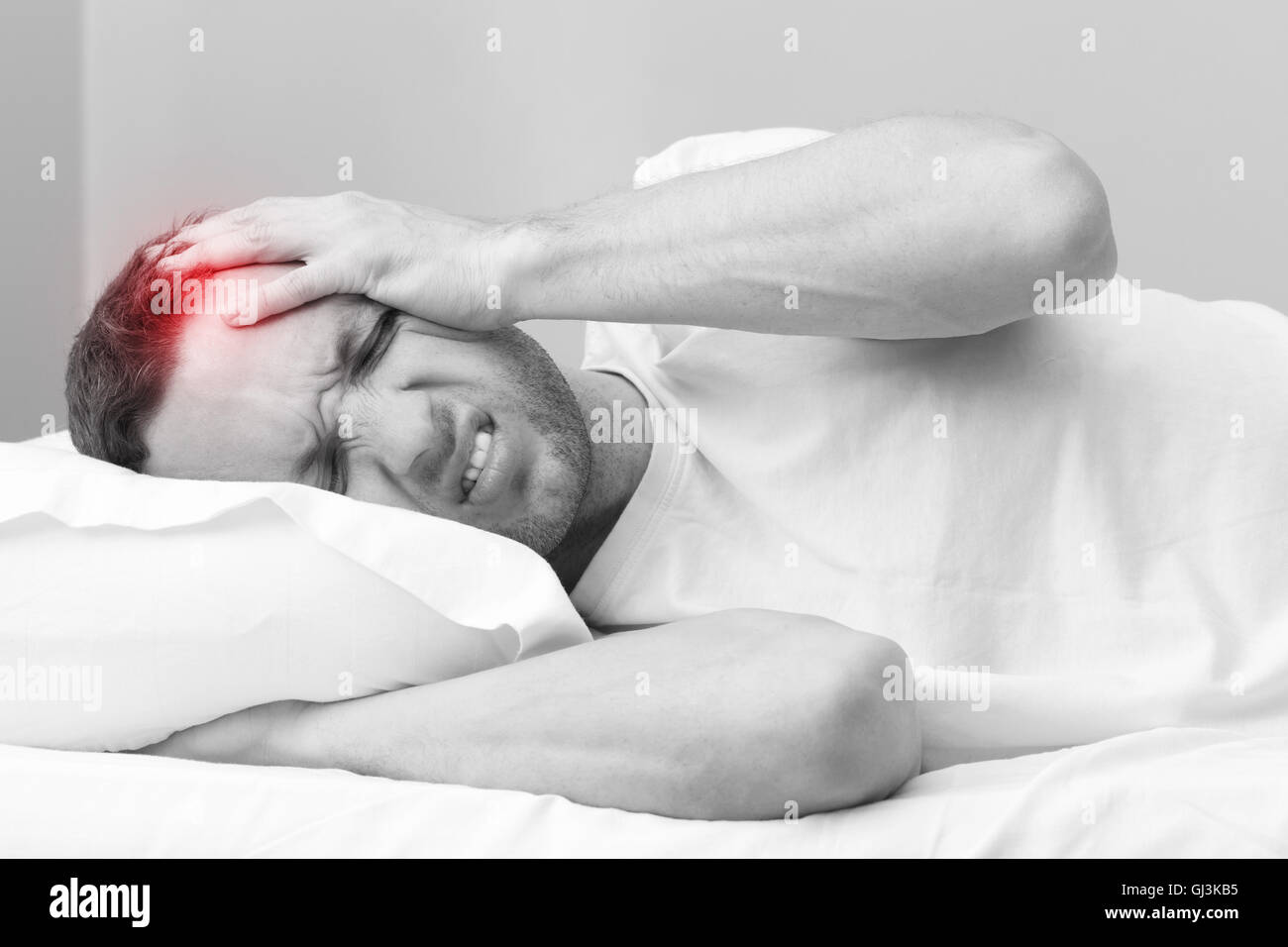 Portrait de jeune homme en colère au lit avec des maux de tête. Noir et blanc photo stylisée avec local spot rouge ache Banque D'Images