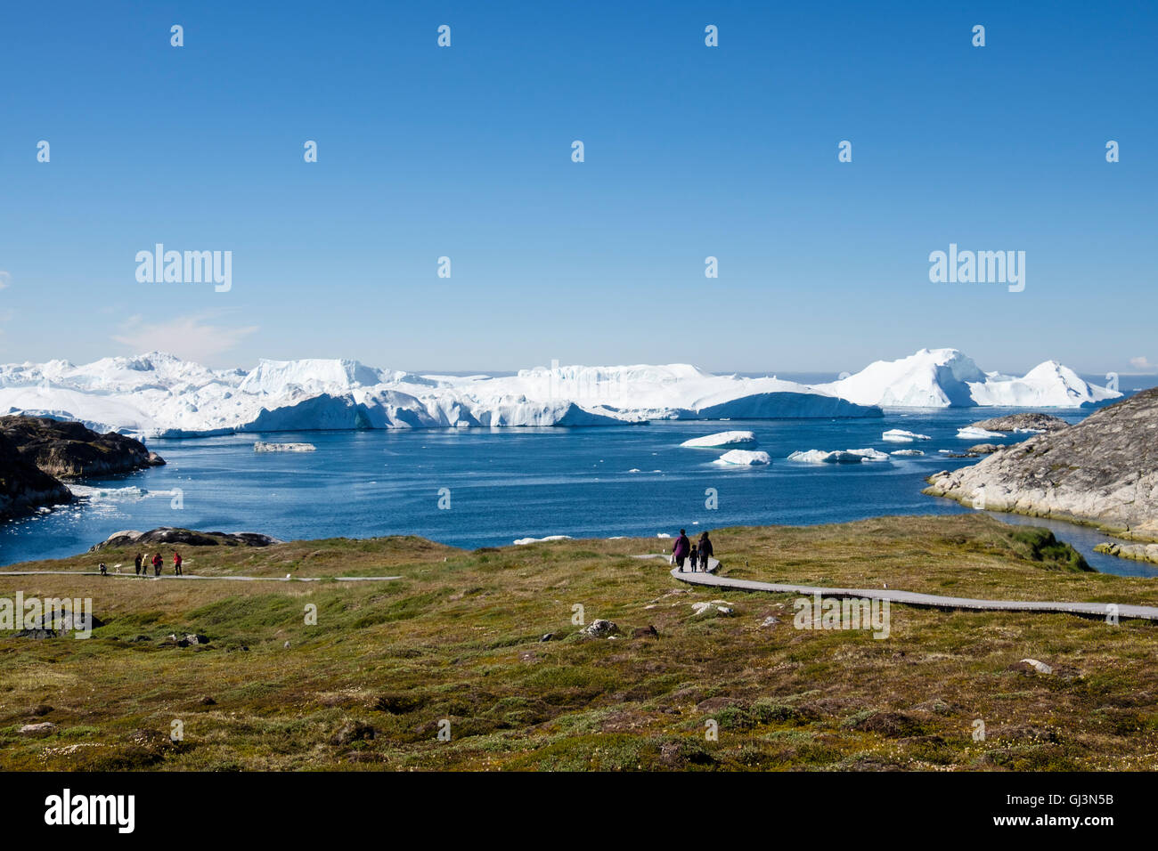 Les gens sur une promenade à travers le règlement des Inuit Sermermiut site archéologique avec des icebergs dans la baie de Disko en été. Groenland Ilulissat Banque D'Images