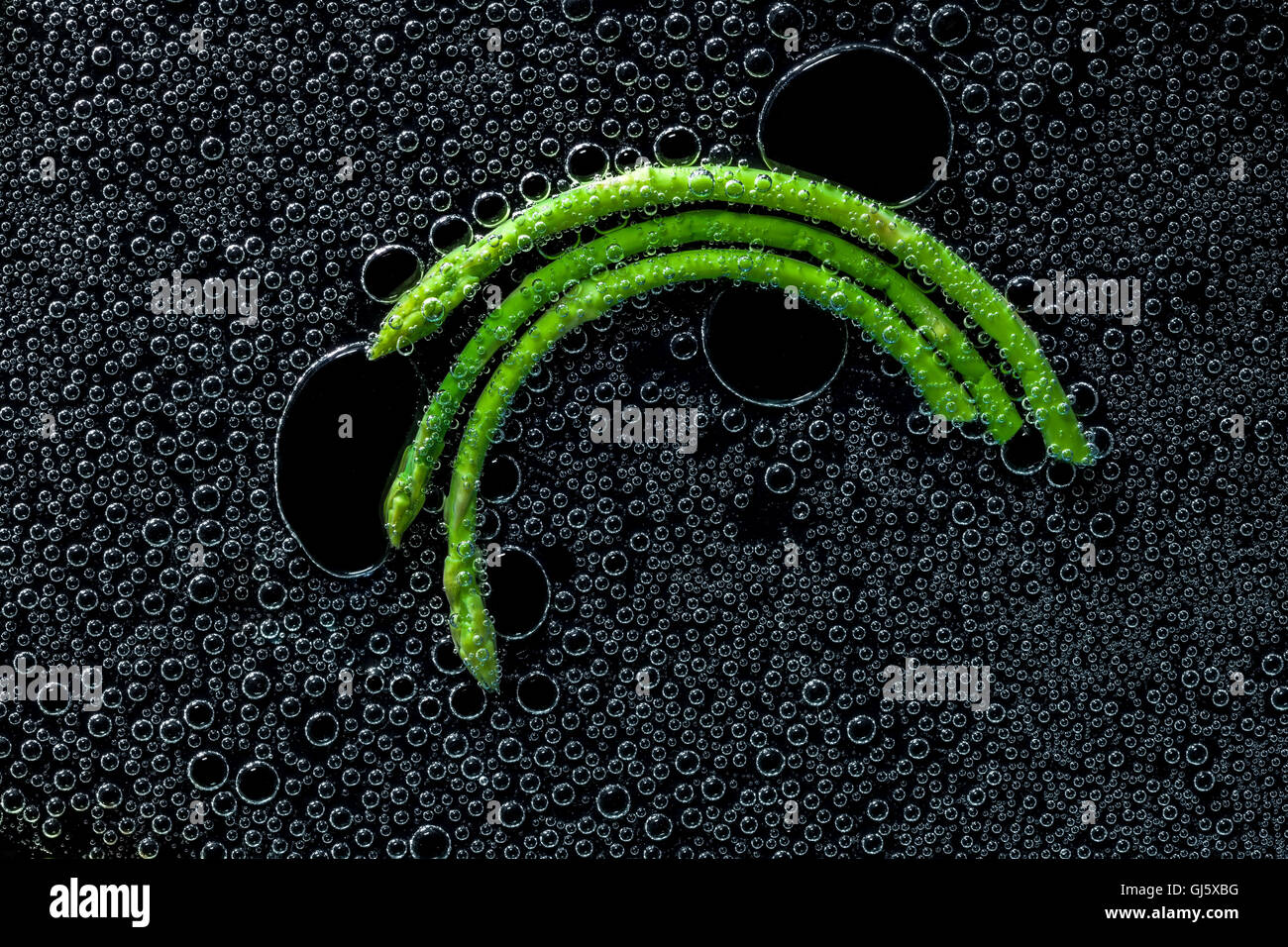 L'asperge verte dans de l'eau minérale, une série de photos. Close-up de l'eau gazéifiée sur fond noir Banque D'Images