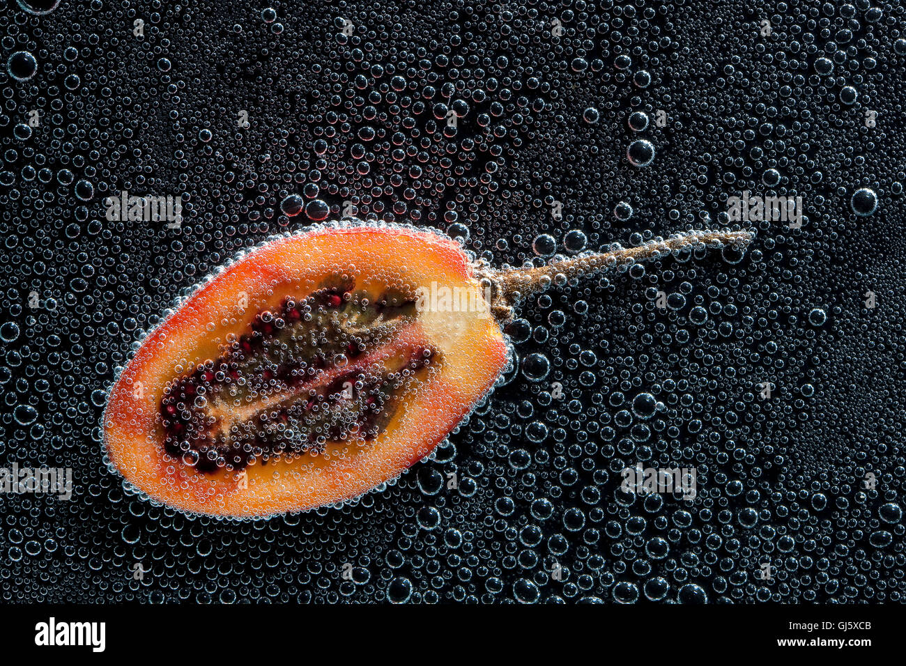 Tamarillo réduit de moitié des fruits dans de l'eau minérale, une série de photos. Close-up de l'eau gazéifiée sur fond noir Banque D'Images