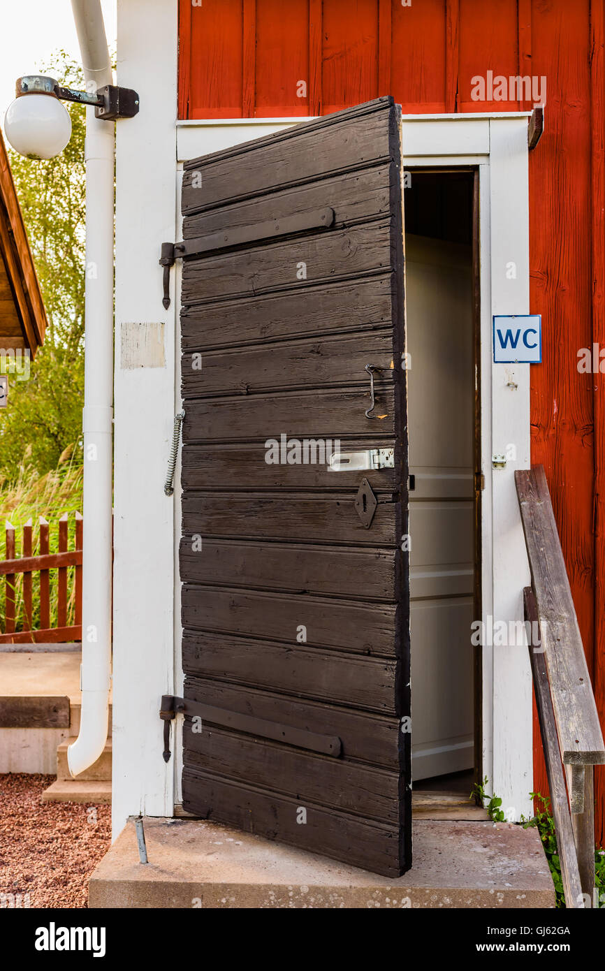 Old weathered et toilettes noir porte en bois à l'angle d'un bâtiment en bois rouge et blanc. Banque D'Images