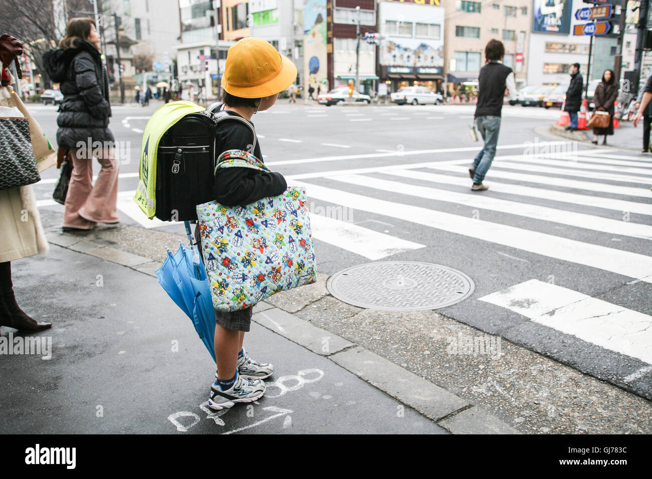 Sur son chemin de retour à la maison par lui-même en voyage de l'école, cet écolier attend, contrairement à tout le monde, à ce croisement pour que les lumières changent à "marche". Tokyo. Banque D'Images