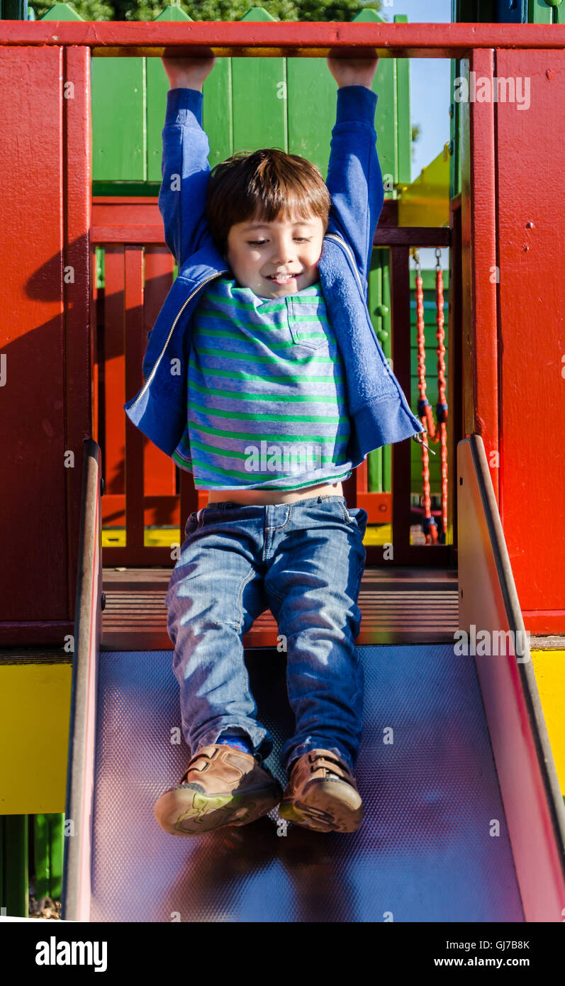 Un jeune garçon joue sur une diapositive dans une aire de jeux pour enfants. Banque D'Images
