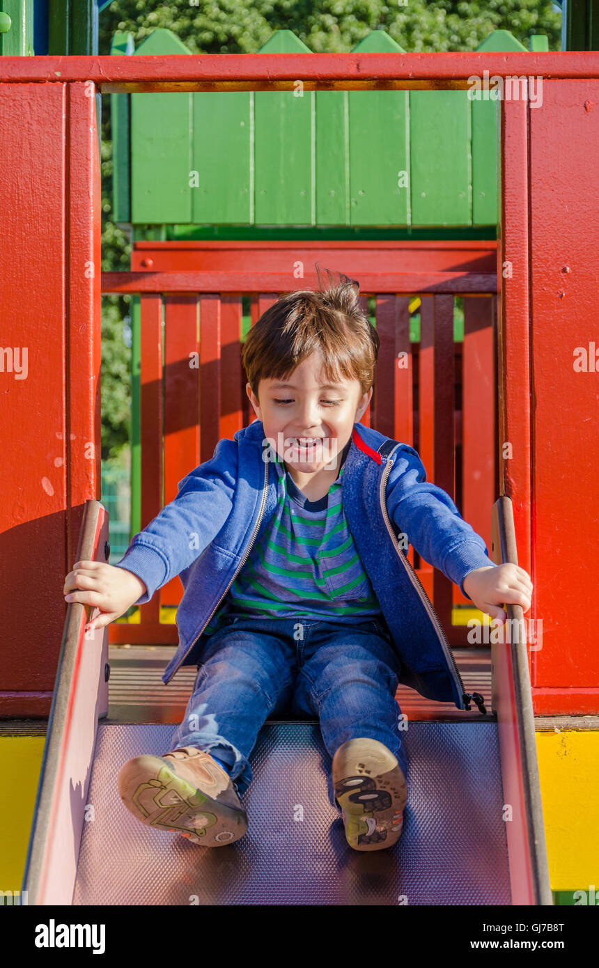 Un jeune garçon joue sur une diapositive dans une aire de jeux pour enfants. Banque D'Images