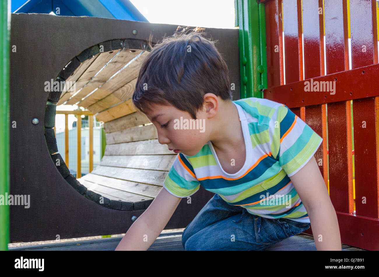 Un jeune garçon joue dans un tunnel à une aire de jeux pour enfants. Banque D'Images