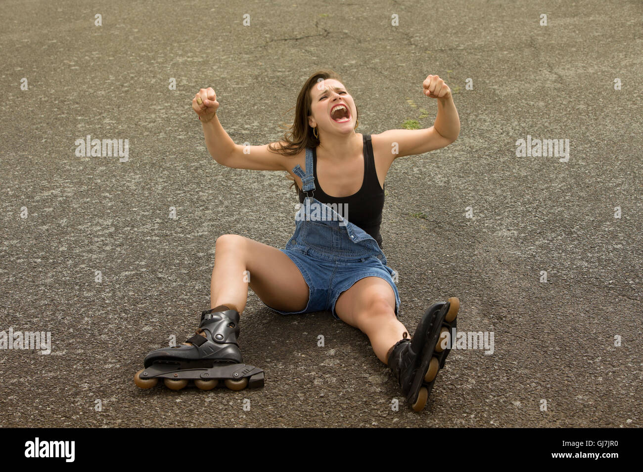 Jeune femme avec des patins assis sur l'asphalte et des cris Banque D'Images