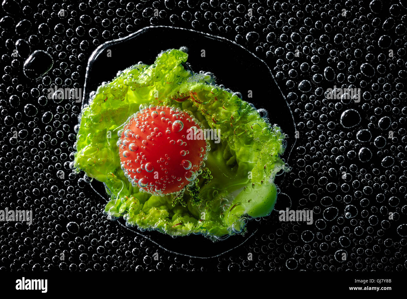 Feuille de salade et la tomate dans l'eau minérale, une série de photos. Close-up de l'eau gazéifiée sur fond noir Banque D'Images