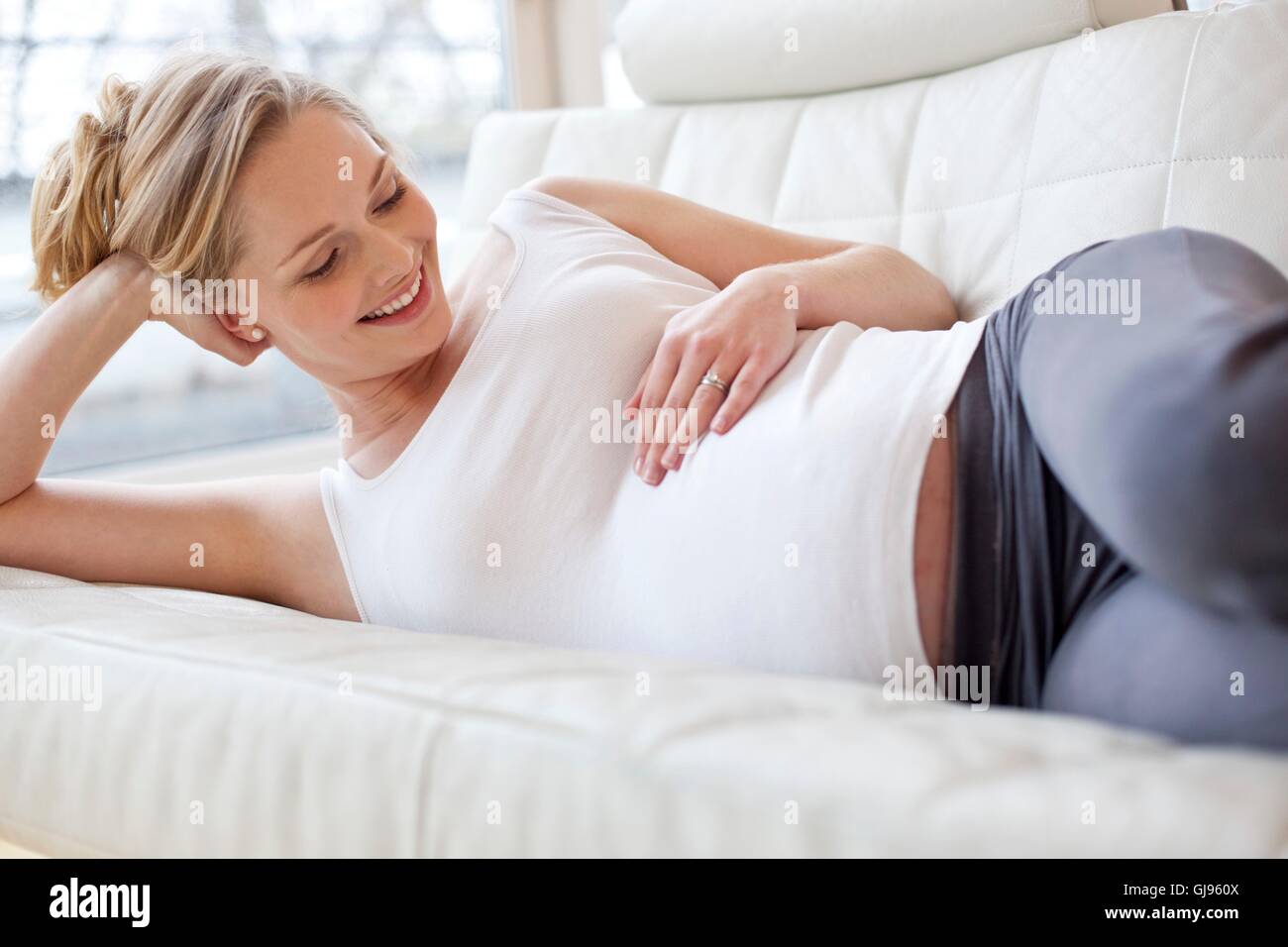 Parution du modèle. Pregnant woman lying on sofa de toucher son ventre. Banque D'Images