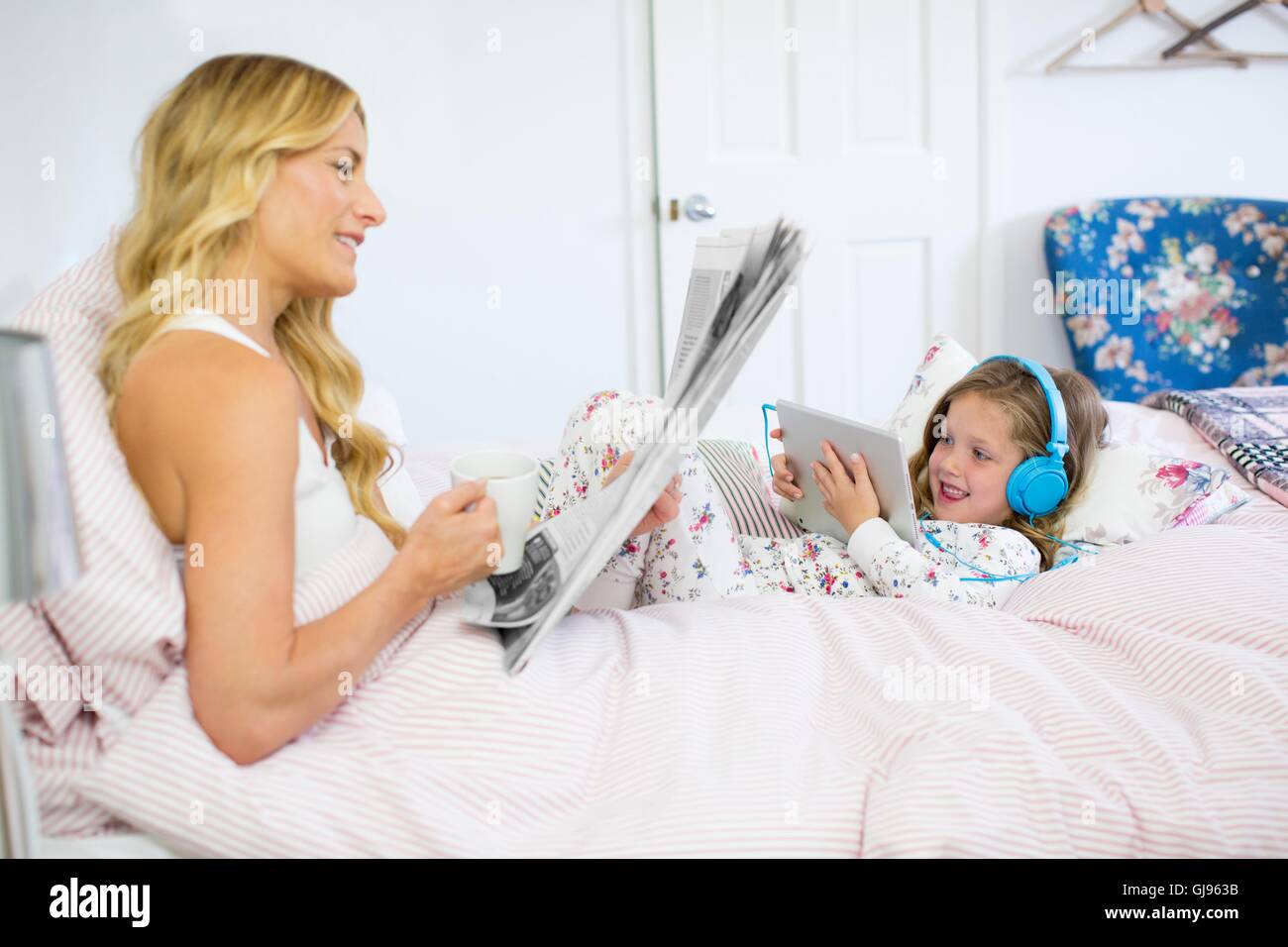 Parution de la propriété. Parution du modèle. Mère et fille au lit avec du papier journal et tablette numérique. Banque D'Images