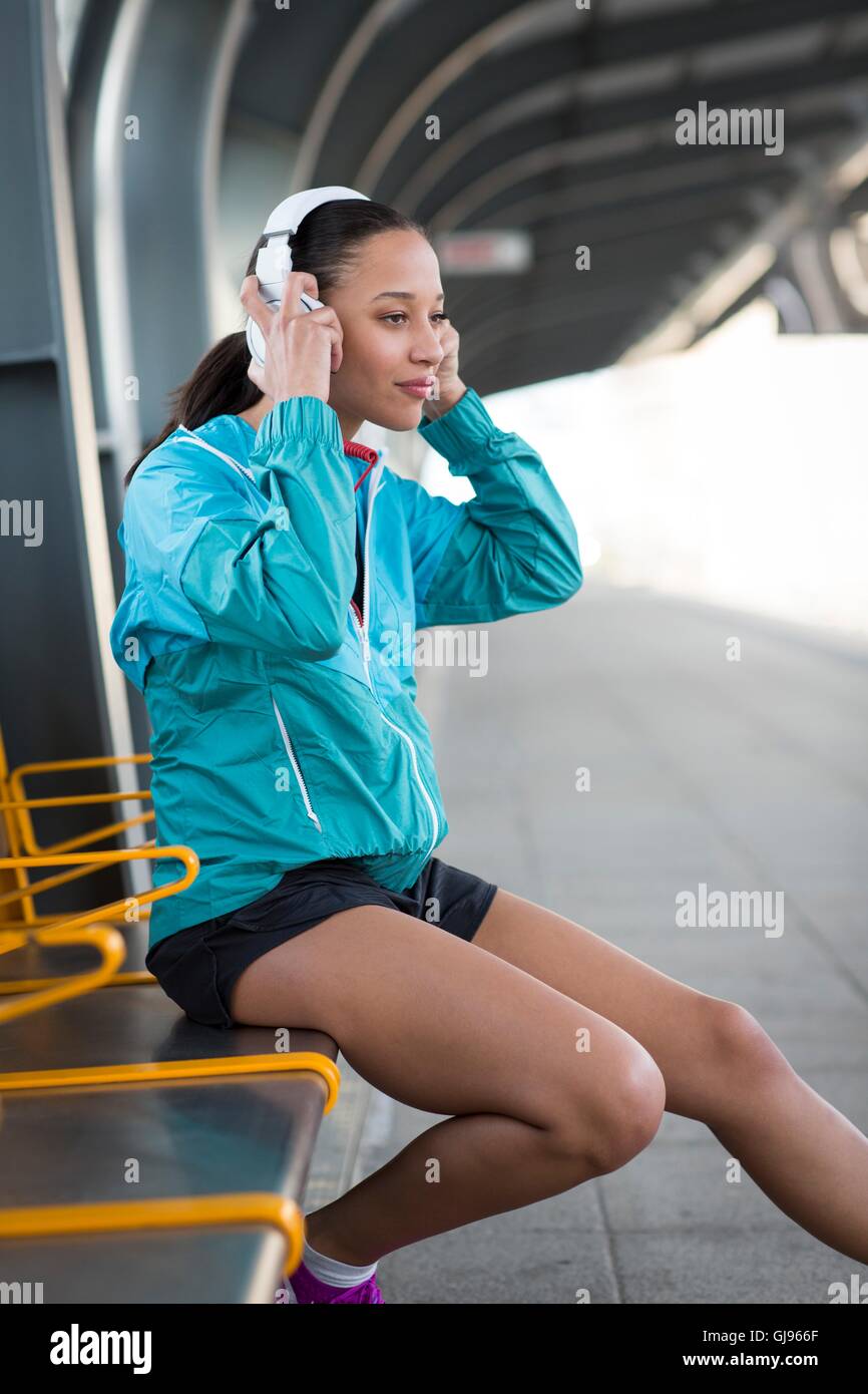 Parution du modèle. Jeune femme assise sur un quai de gare portant des écouteurs. Banque D'Images