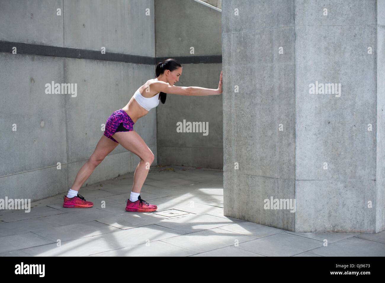 Parution du modèle. Young woman stretching contre mur. Banque D'Images
