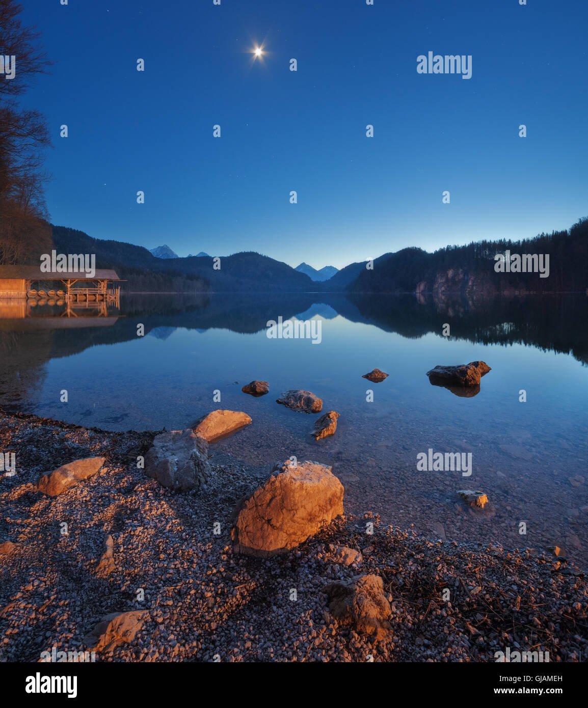 Nuit dans le lac Alpsee en Allemagne. Beau paysage avec lac, montagne, forêt, étoile, pleine lune, ciel bleu et des pierres Banque D'Images