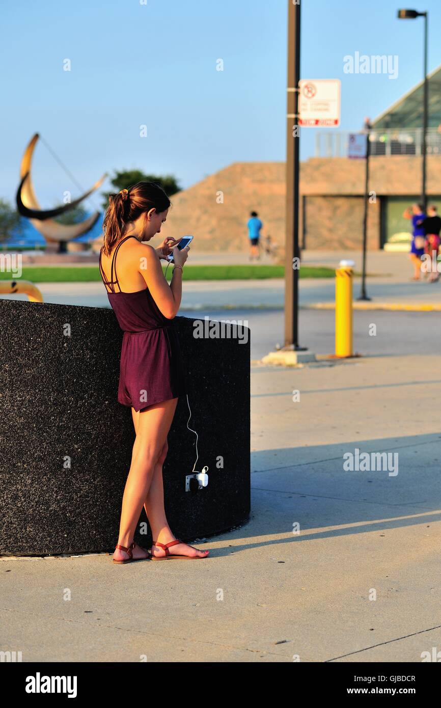Une jeune femme profite d'une piscine prise électrique pour recharger son téléphone portable tout en utilisant l'appareil. Chicago, Illinois, USA. Banque D'Images