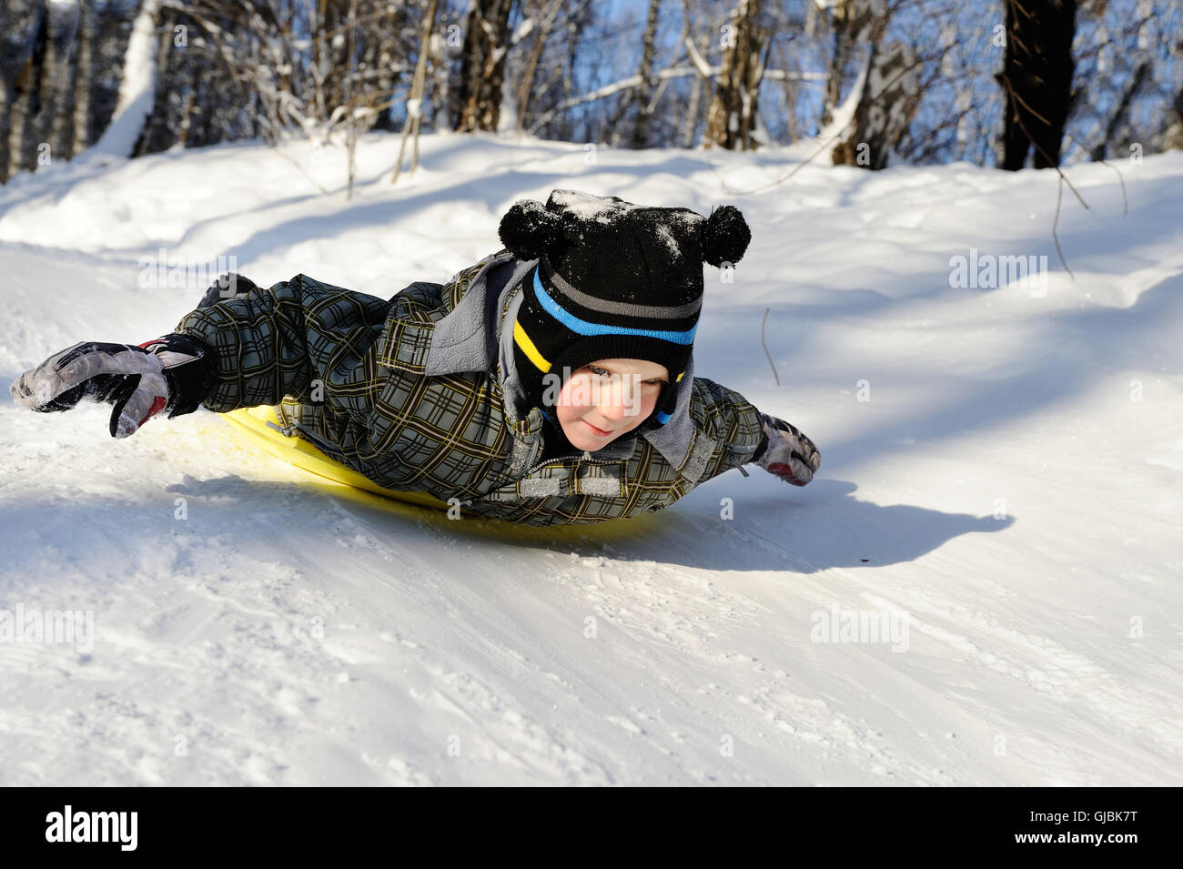 Petit garçon équitation avec des collines sur les traîneaux sur l'hiver Banque D'Images