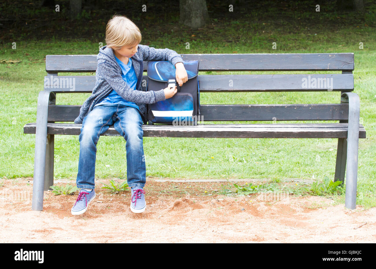 Smiling little boy ouvrant son sac à dos. Enfant assis sur un banc en bois. Piscine en plein air. L'éducation, les concept Banque D'Images