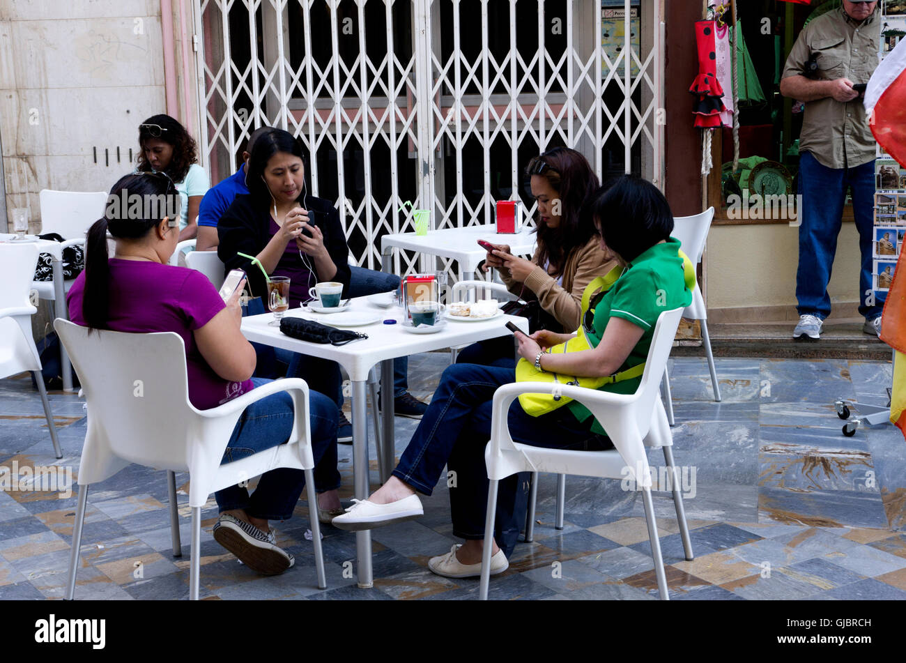 4 filles asiatiques vérifier leurs téléphones intelligents au café en plein air, tout en prenant un verre. Banque D'Images