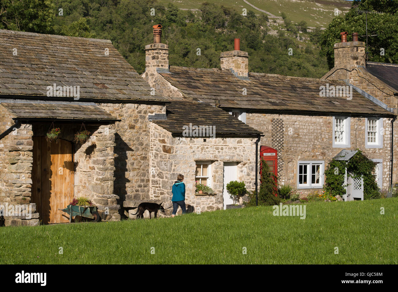 Lady dog walking, passe pittoresque, stone cottages à Arncliffe, un joli village, dans le Yorkshire Dales National Park, England. Banque D'Images