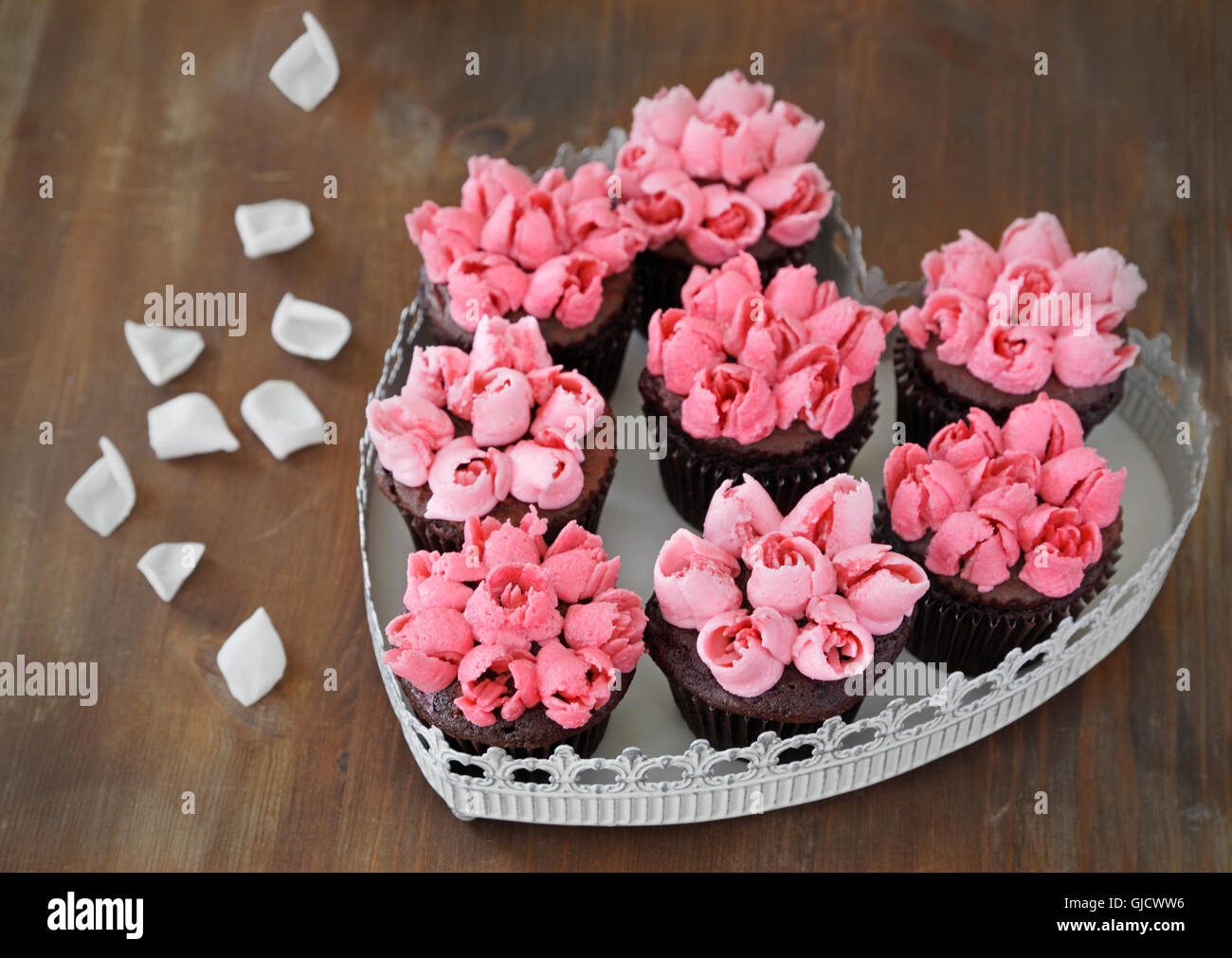 Cupcakes. Petits gâteaux au chocolat avec crème au beurre vanille rose rose dans une assiette en forme de coeur Banque D'Images