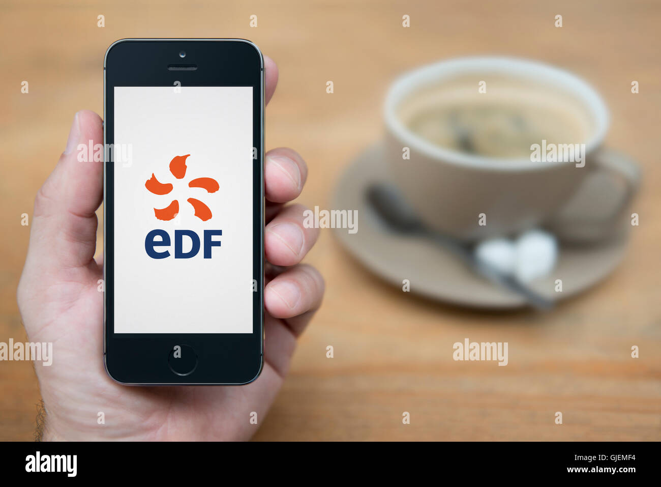 Un homme se penche sur son iPhone qui affiche le logo d'EDF, alors qu'assis avec une tasse de café (usage éditorial uniquement). Banque D'Images