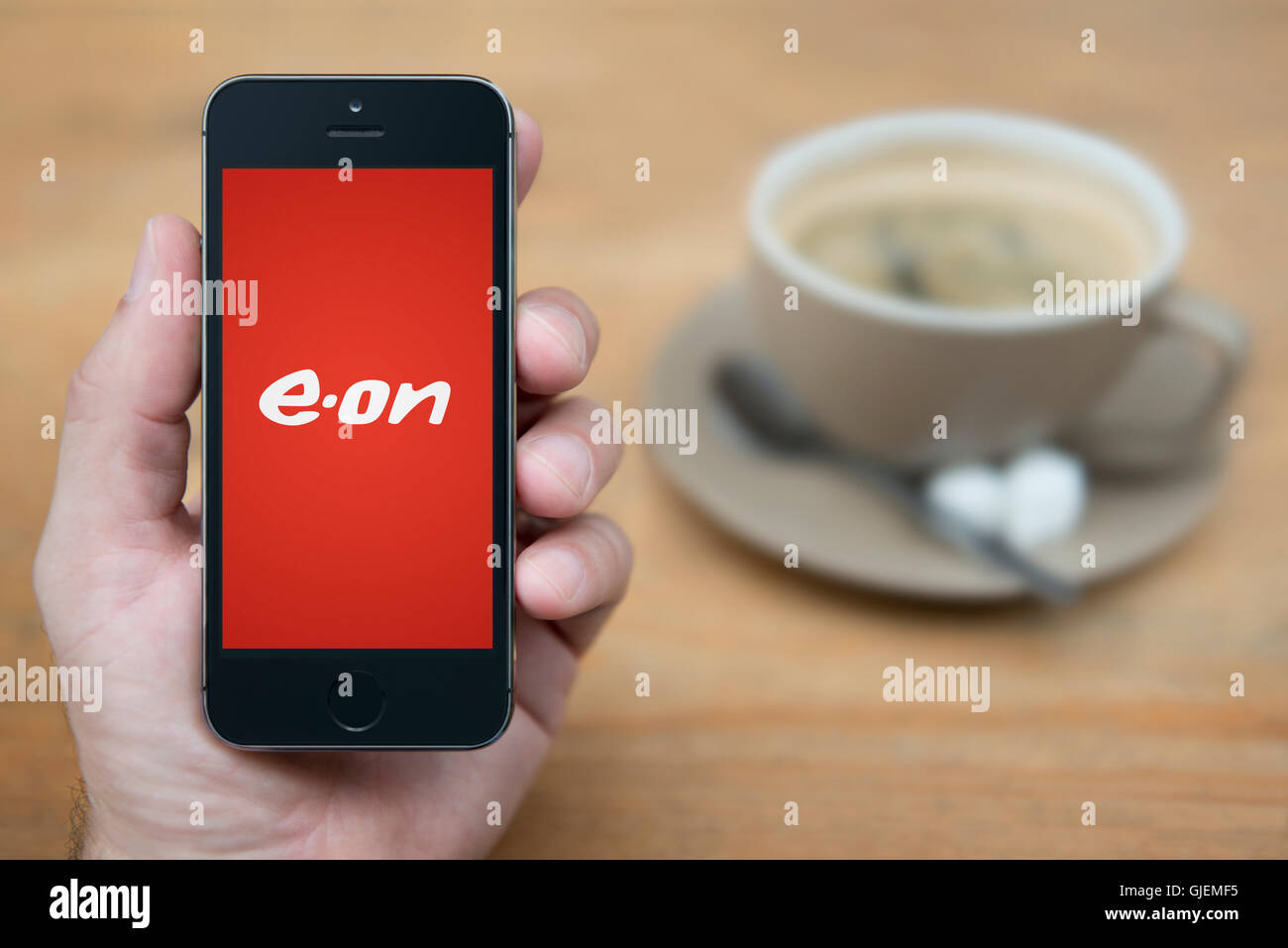 Un homme se penche sur son iPhone qui affiche le logo d'E.On, alors qu'assis avec une tasse de café (usage éditorial uniquement). Banque D'Images