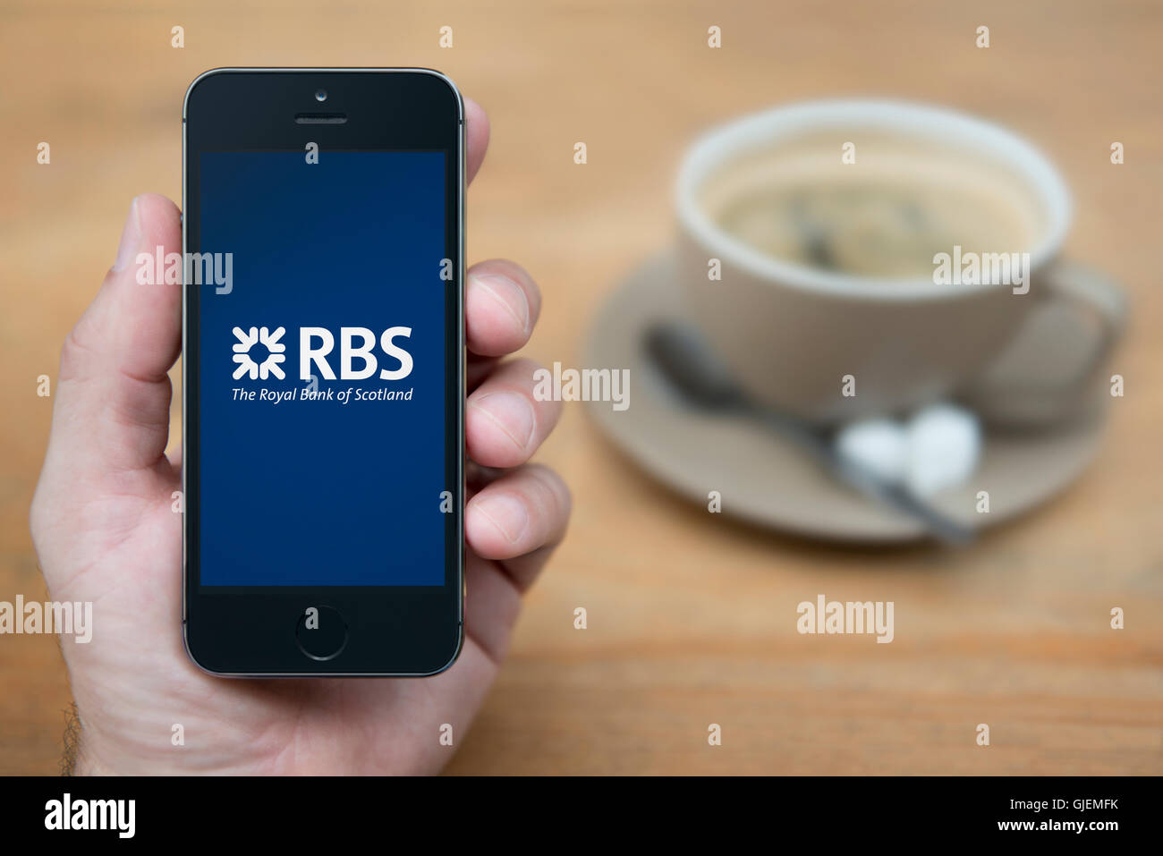 Un homme se penche sur son iPhone qui affiche le logo RBS, tandis qu'assis avec une tasse de café (usage éditorial uniquement). Banque D'Images