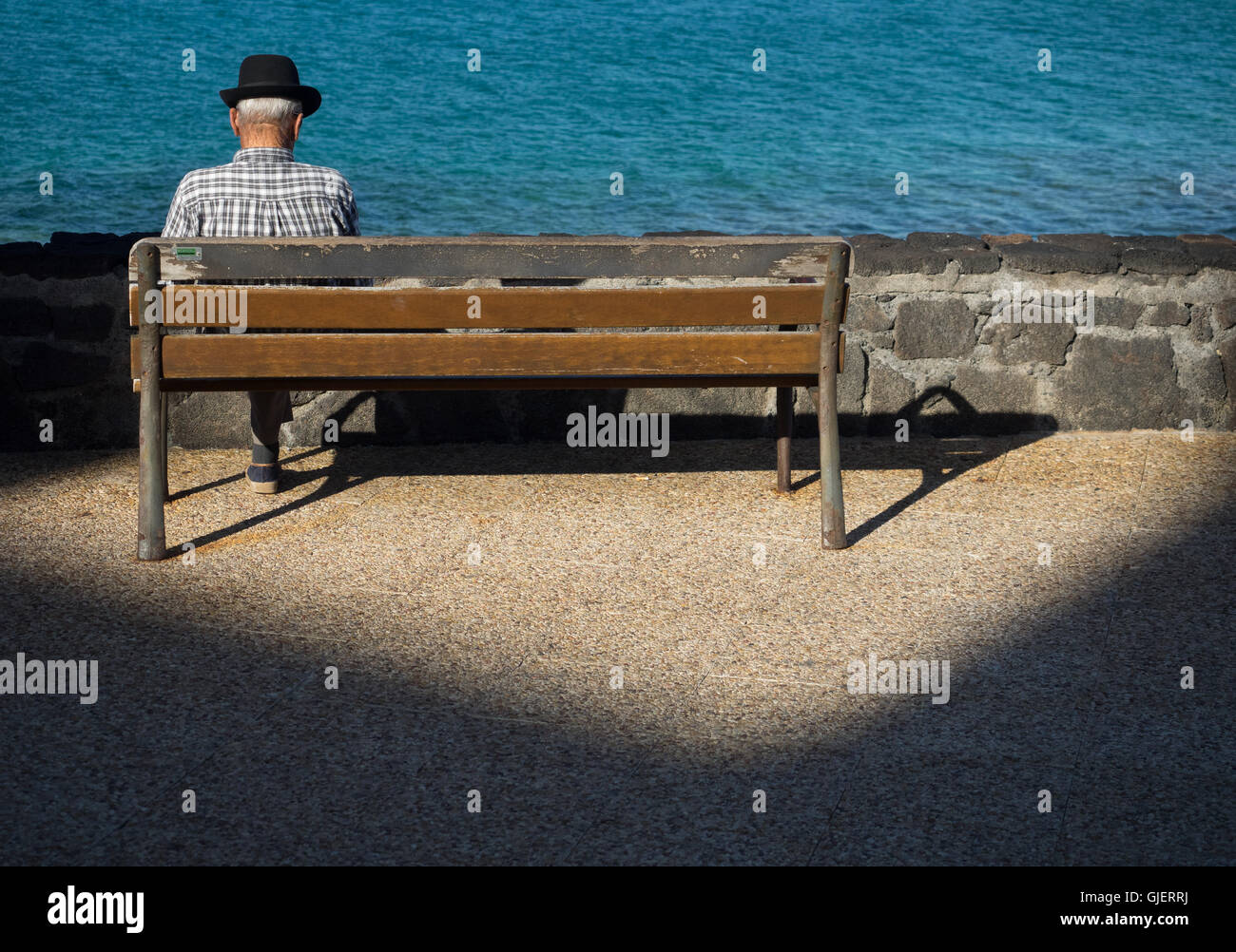 Vieux homme seul assis seul sur un banc en bois sur une promenade en bord de mer en été Banque D'Images