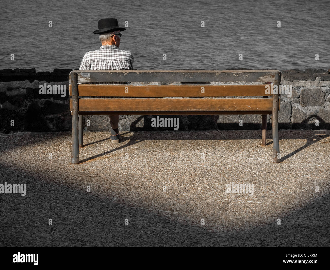 Vieux homme seul assis seul sur un banc en bois sur une promenade en bord de mer en été Banque D'Images