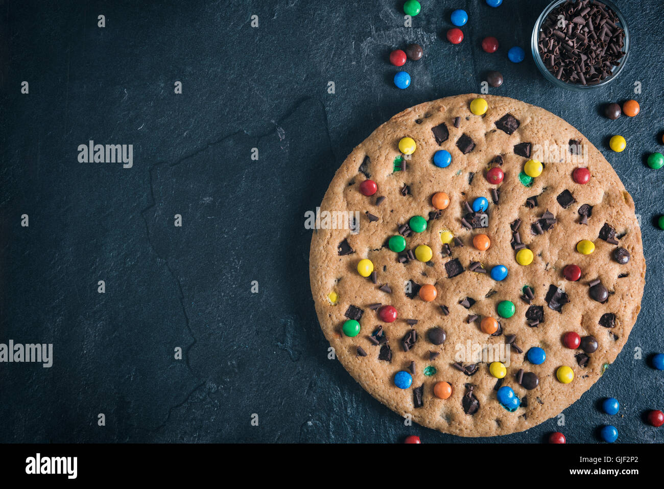 Big chocolate chip cookie fait maison avec bonbons colorés sur fond sombre,espace blanc Banque D'Images