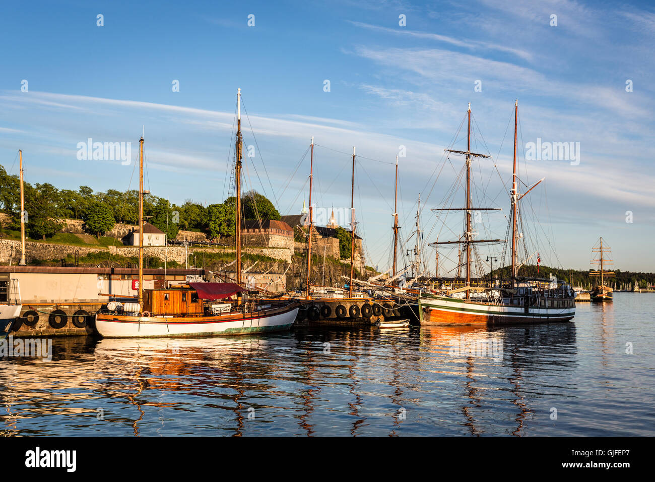 Coucher de soleil sur le port d'Oslo avec beaucoup de vieux voiliers en bois et la forteresse Akershus en arrière-plan dans la capitale de la Norvège. Banque D'Images