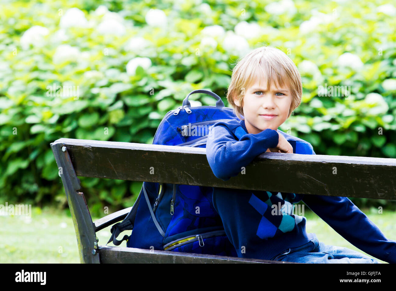 Petit garçon assis sur un banc en bois avec son sac à dos. L'éducation, l'école, de vie, de personnes concept Banque D'Images