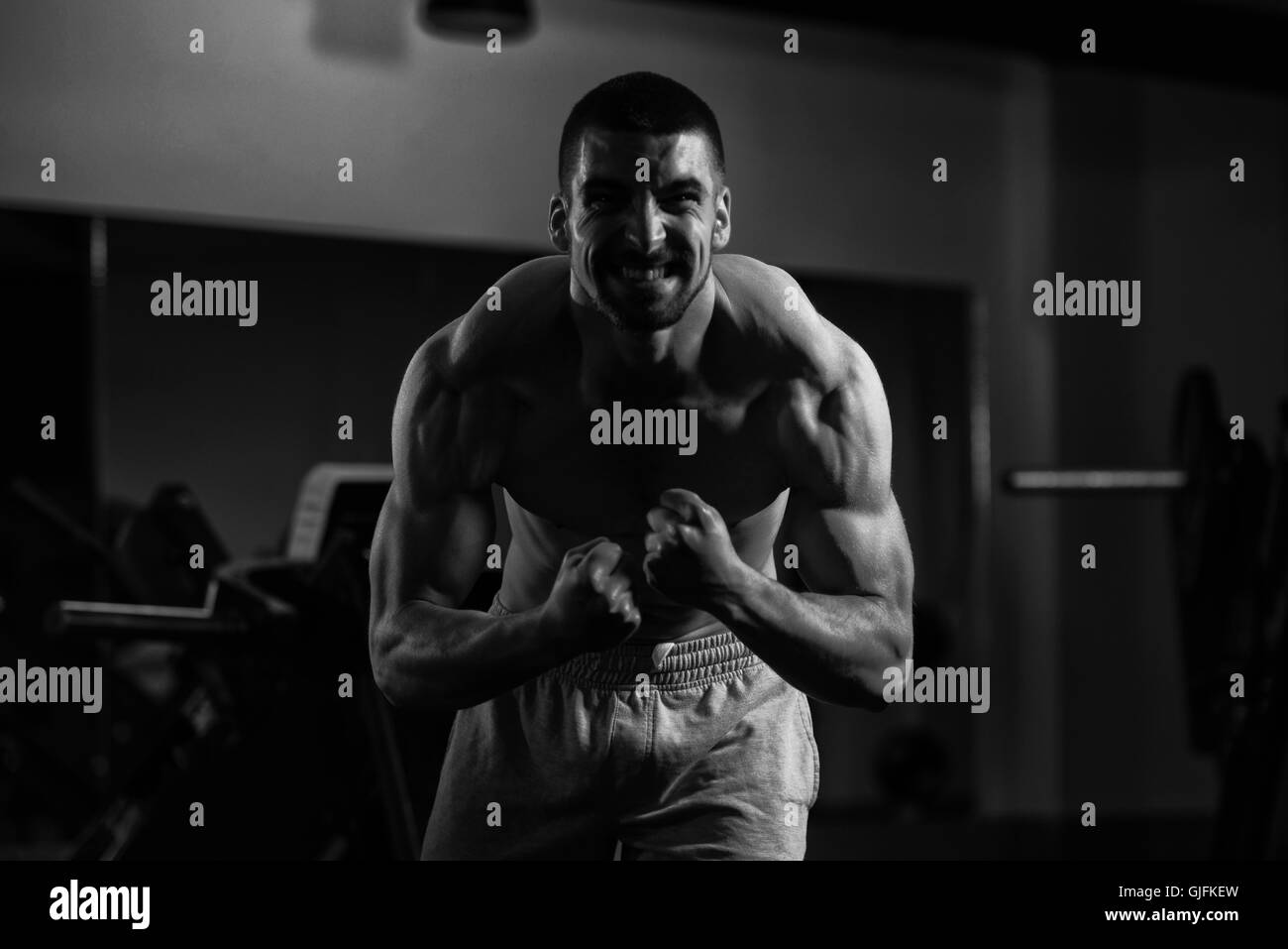 Jeune homme debout forte dans la salle de sport et Flexing Muscles musculaire - Fitness Model Posing Bodybuilder athlétiques exercices après Banque D'Images