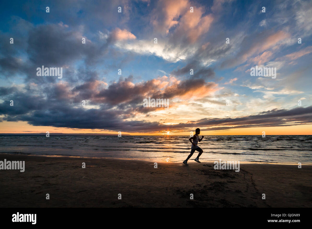 Un homme qui court au coucher du soleil sur la plage Wasaga. Banque D'Images