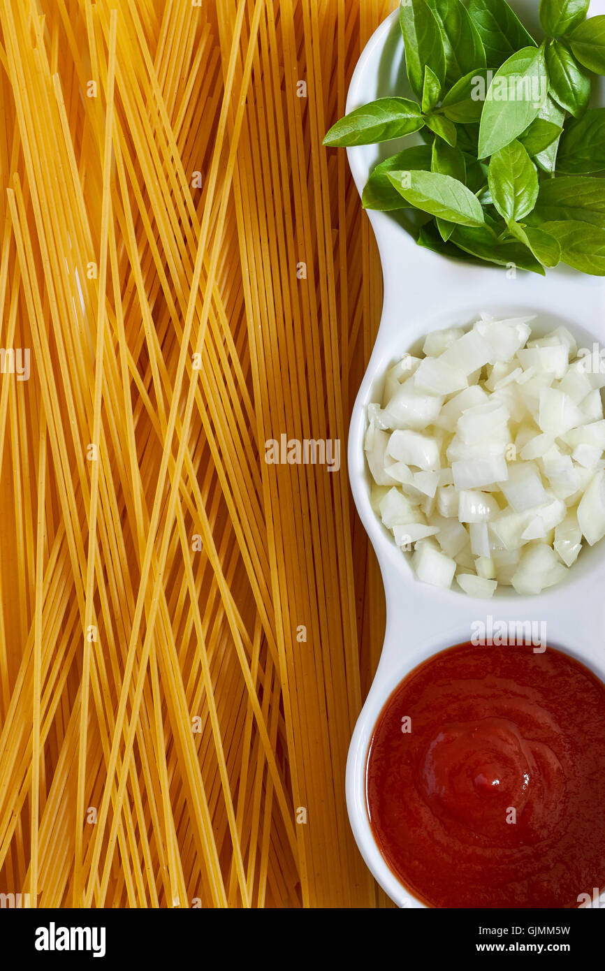 Le basilic, oignons tranchés et la pâte de tomate dans un bol blanc avec des spaghettis éparpillés. Image Concept pour la cuisine italienne. Haut Banque D'Images