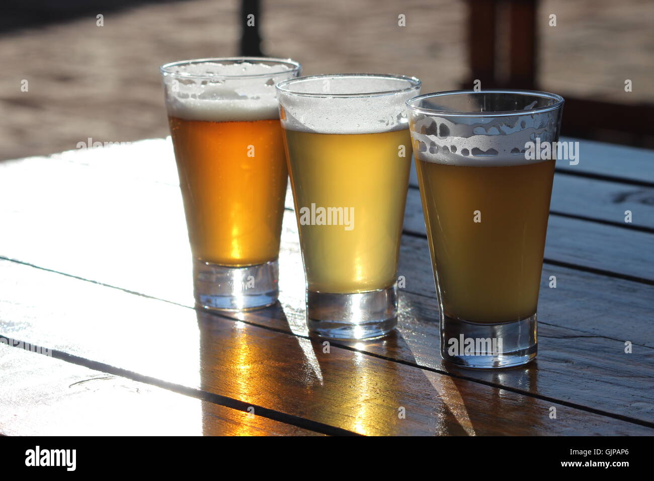 Une sélection de bières artisanales de trois au cours d'une dégustation sur une table en bois avec le soleil qui brille dans les verres Banque D'Images