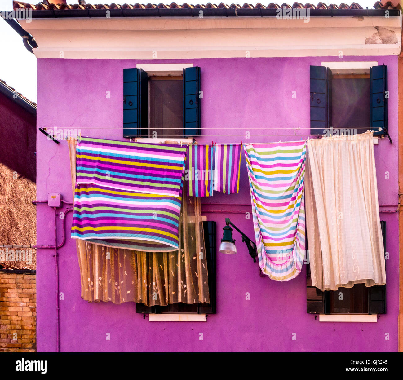 Maison peinte en violet avec linge rayé coloré suspendu à l'extérieur sur les lignes de lavage. Île de Burano. Venise, Italie Banque D'Images
