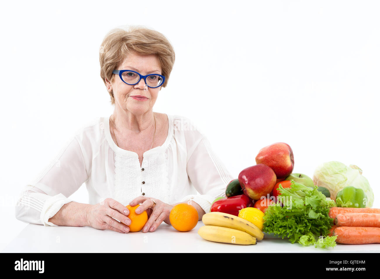 Aîné heureux Caucasian woman holding hands deux oranges, les légumes et les fruits sont sur la table, fond blanc Banque D'Images