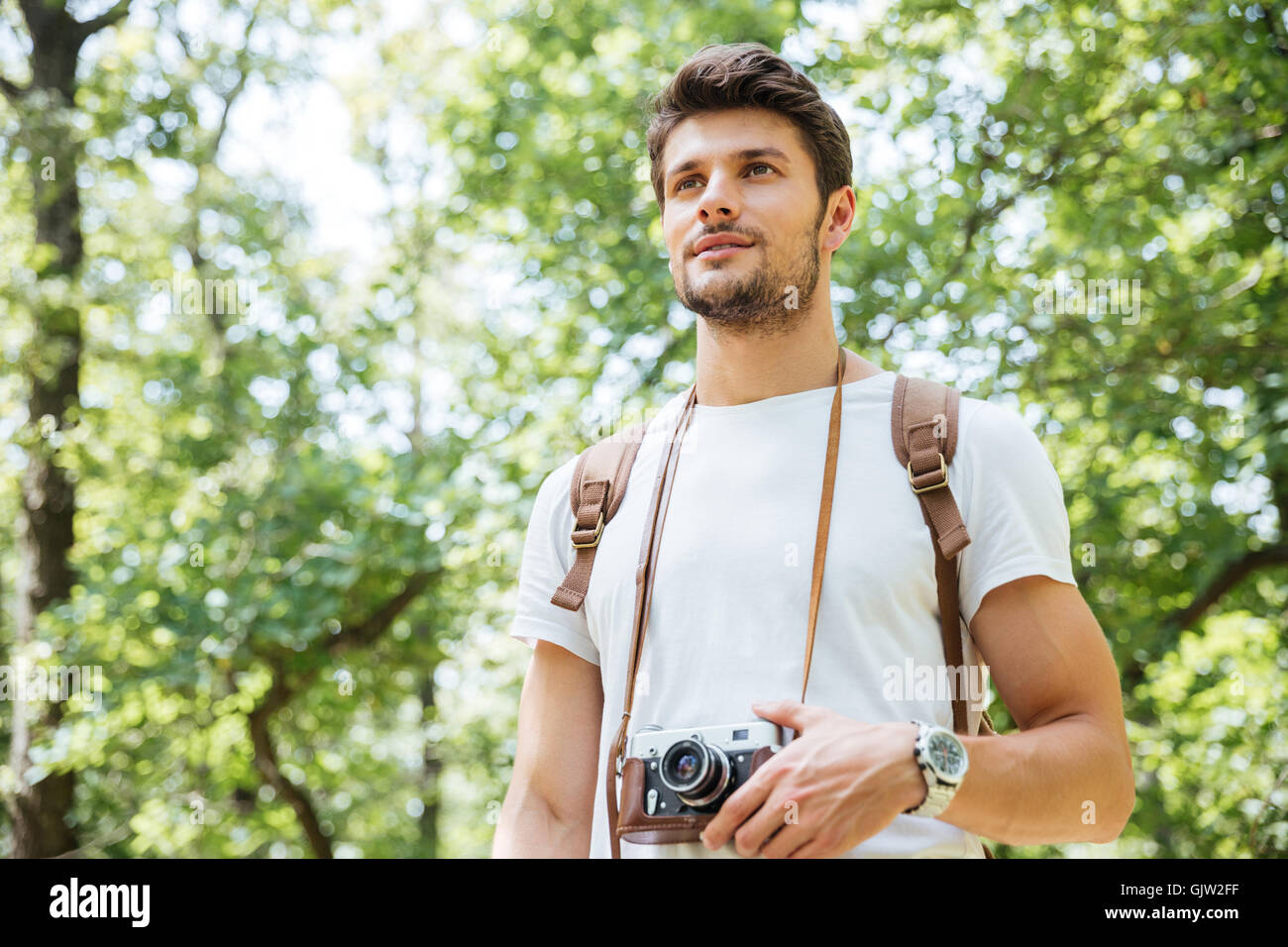 Beau jeune homme avec sac à dos et appareil photo ancien standing in forest Banque D'Images