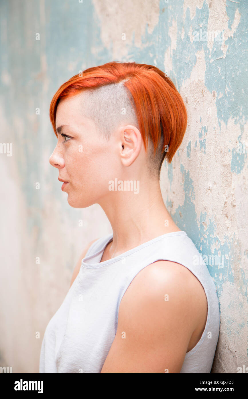 Jeune femme cheveux rouge moderne avec côté hairstlye rasée par le vieux mur permanent Banque D'Images