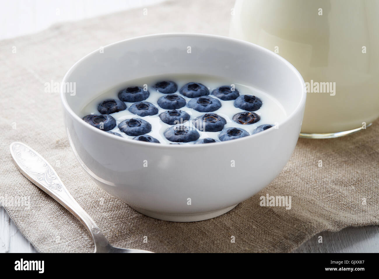 Bol de bleuets frais avec du lait servi sur table en bois blanc Banque D'Images