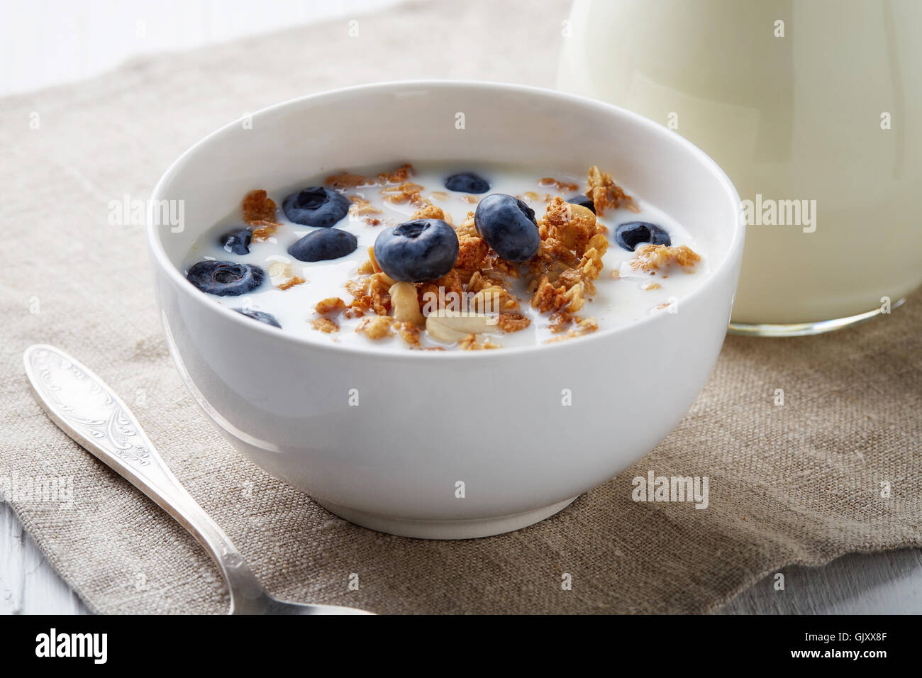 Bol de céréales à grains entiers avec des bleuets et du lait sur la table en bois blanc Banque D'Images