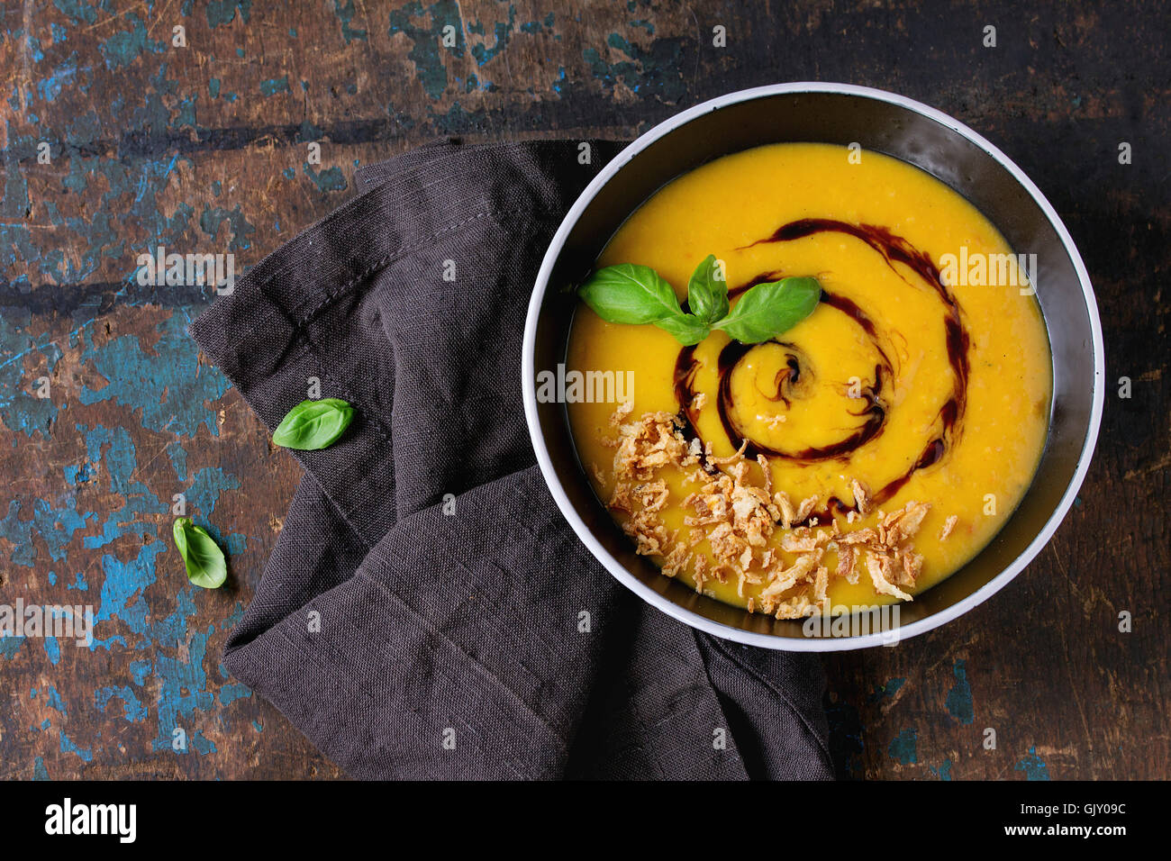 Bol en céramique noire de la citrouille et pommes de terre soupe à la crème avec le basilic, l'oignon frit et sauce balsamique, servi sur les textiles na Banque D'Images