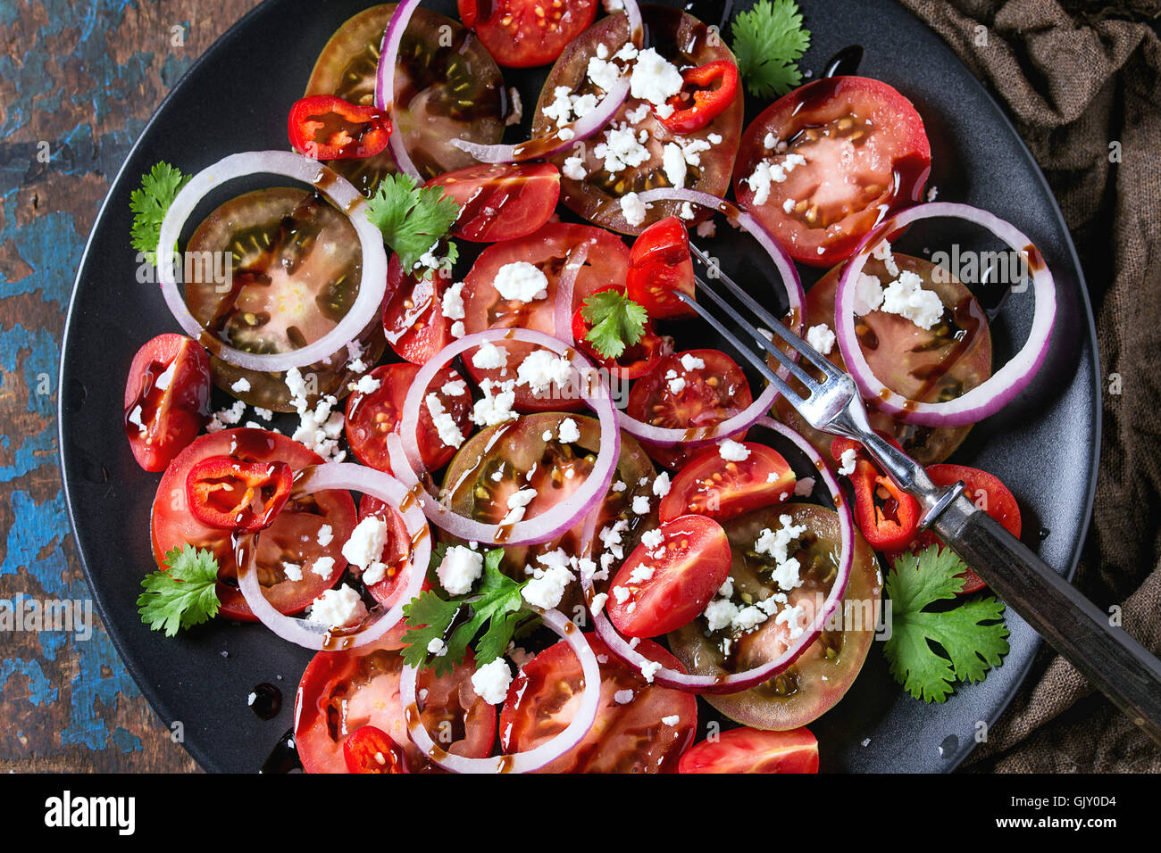 Plaque noire avec des tranches de tomates différentes, l'oignon rouge, vinaigre balsamique, le persil et sause fromage feta salade, servi avec la fourchette sur humide sa Banque D'Images