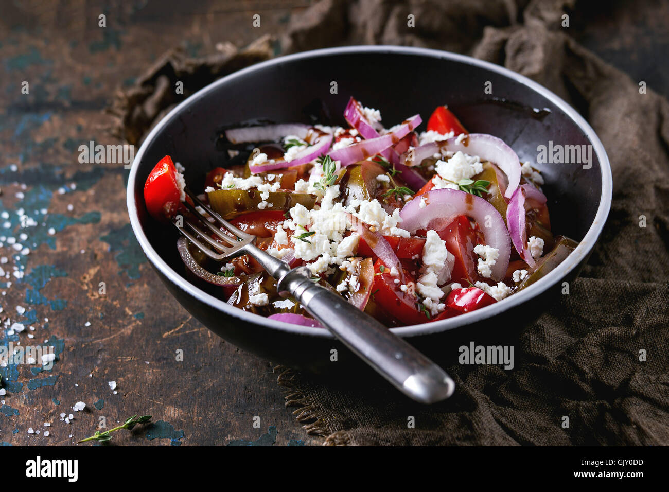 Bol noir avec des tranches de tomates différentes, l'oignon rouge, vinaigre balsamique, de thym et de sause fromage feta salade, servi avec une fourchette sur les sackc Banque D'Images