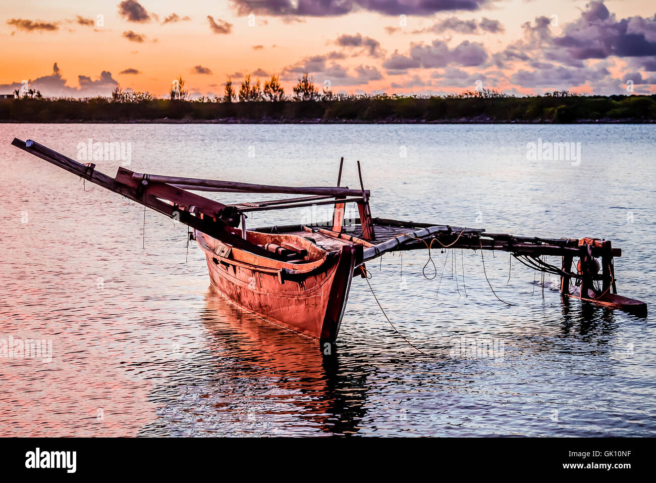 Un canot de la Micronésie en bois ancré dans la baie au coucher du soleil. Banque D'Images