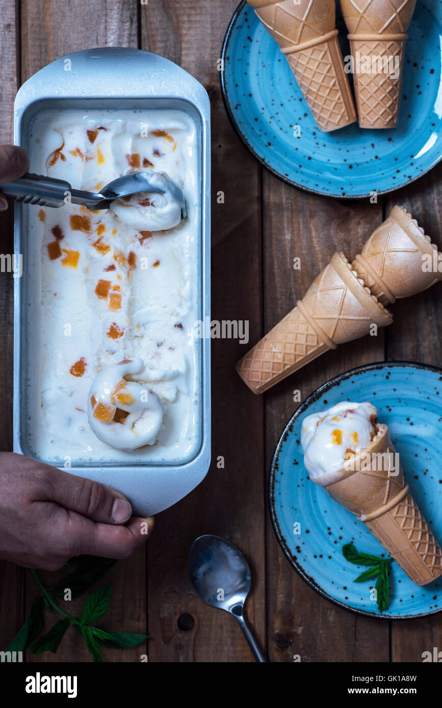 Une femme est l'écopage peach ice cream à partir de la casserole et le servir avec ice cream cones sur deux plaques bleues. Banque D'Images