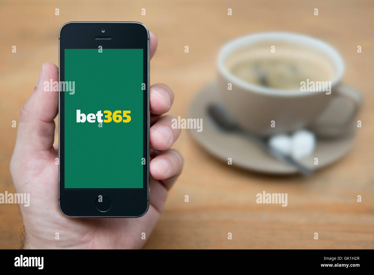 Un homme se penche sur son iPhone qui affiche le logo de Bet365, alors qu'assis avec une tasse de café (usage éditorial uniquement). Banque D'Images