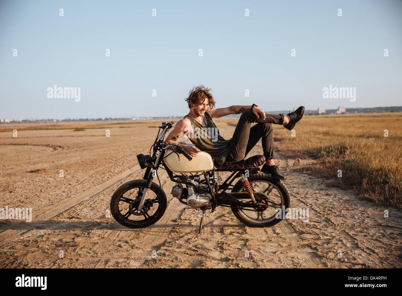 Jeune homme brutal portant sur sa moto dans le désert et posing Banque D'Images