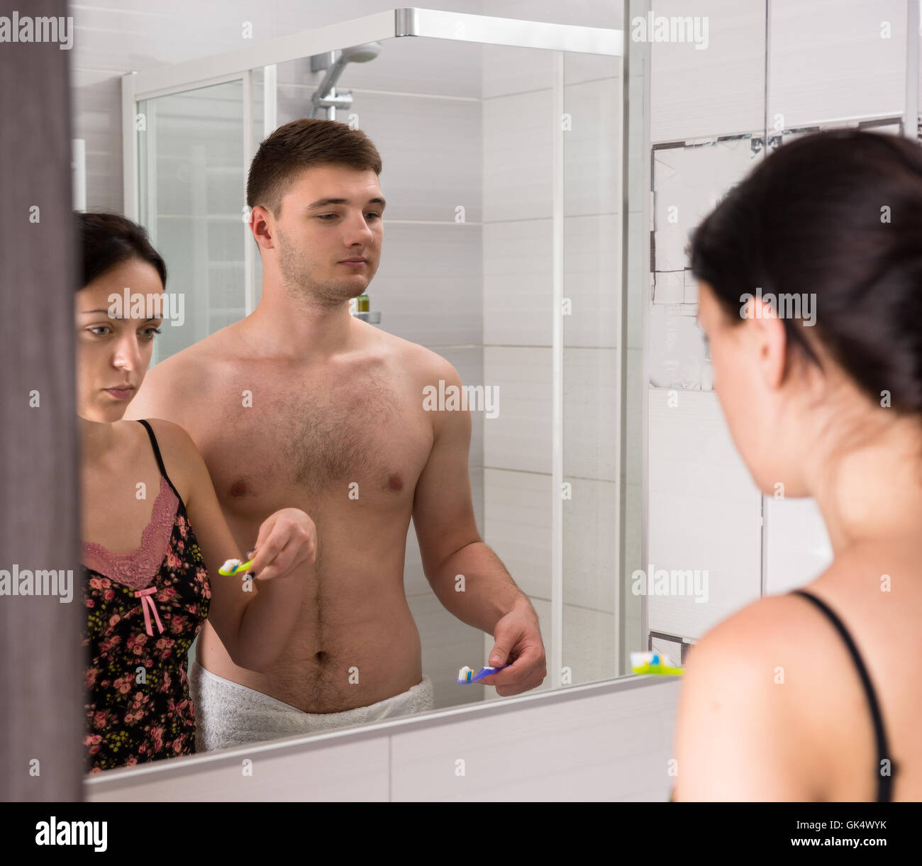 Jeune couple vont se brosser les dents, debout devant un miroir dans la salle de bains moderne carrelée Banque D'Images