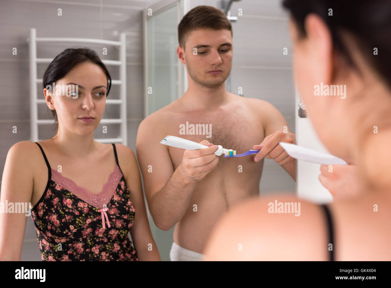 Beau couple vont se brosser les dents, debout devant un miroir dans la salle de bains moderne carrelée Banque D'Images